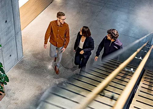 Kolme henkilöä kävelee ja keskustelee toimistolla